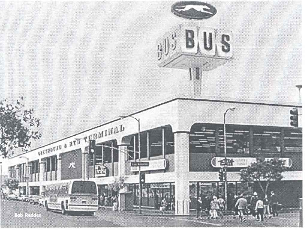 pedestrians cross the street as a bus drives next to the bus terminal building