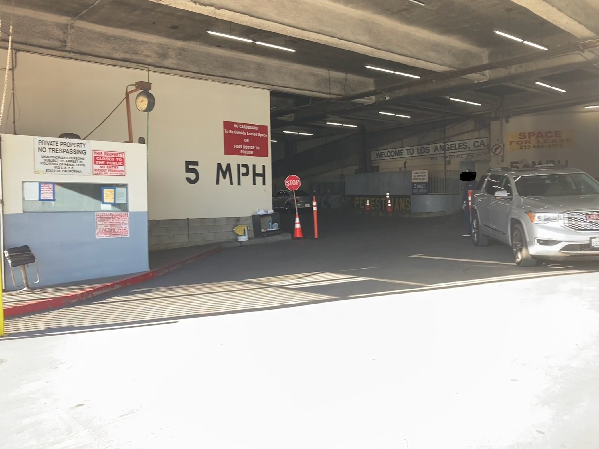 entrance to parking inside the Mart. The walls have 5 MPH speed limit stencilled on, and the ceiling slopes prominently downward to the left. several signs prohibit pedestrians, and one welcomes you to los angeles, CA