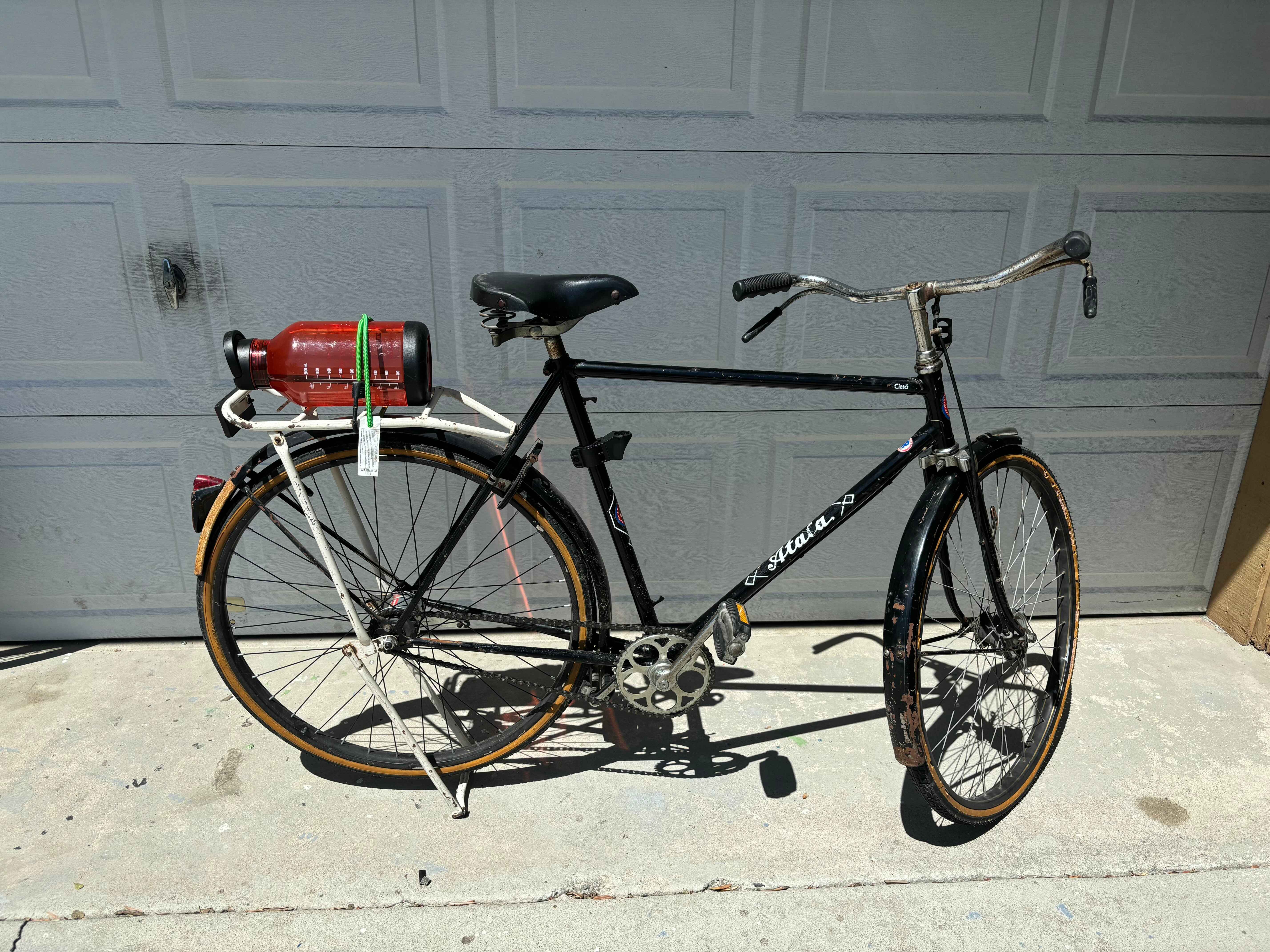 bike in front of garage door, with large water bottle bungee corded to the rear rack