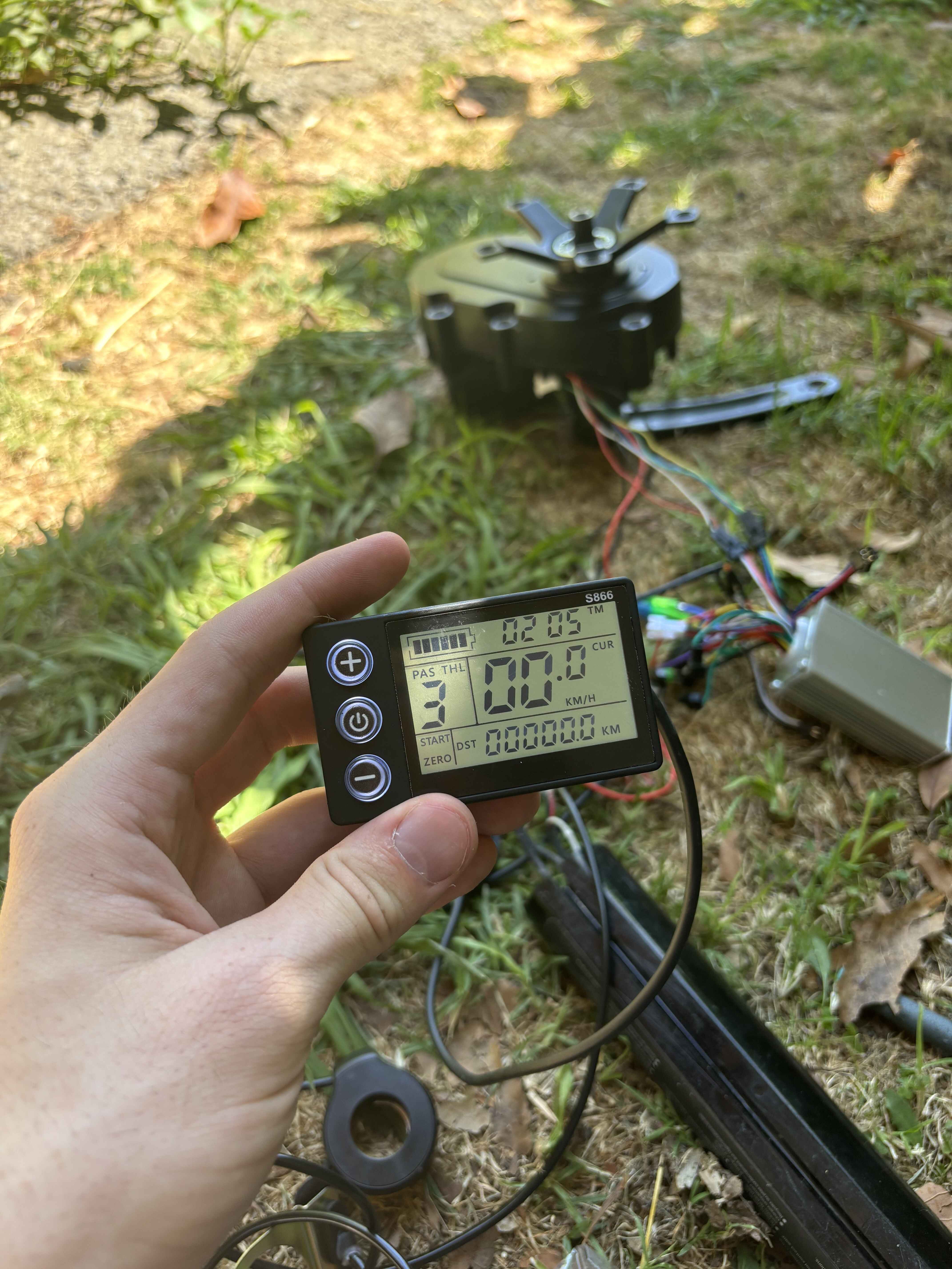 holding a small lcd screen in hand. battery, controller and motor in the background