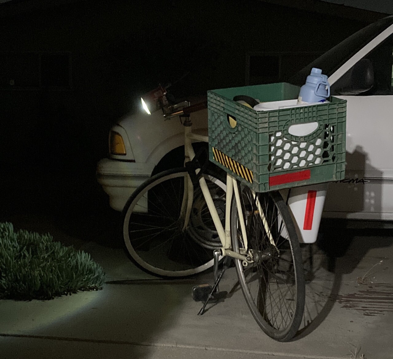 single speed bike with crate and bucket mounted to a rear rack, and the cantern shining majestically in the night