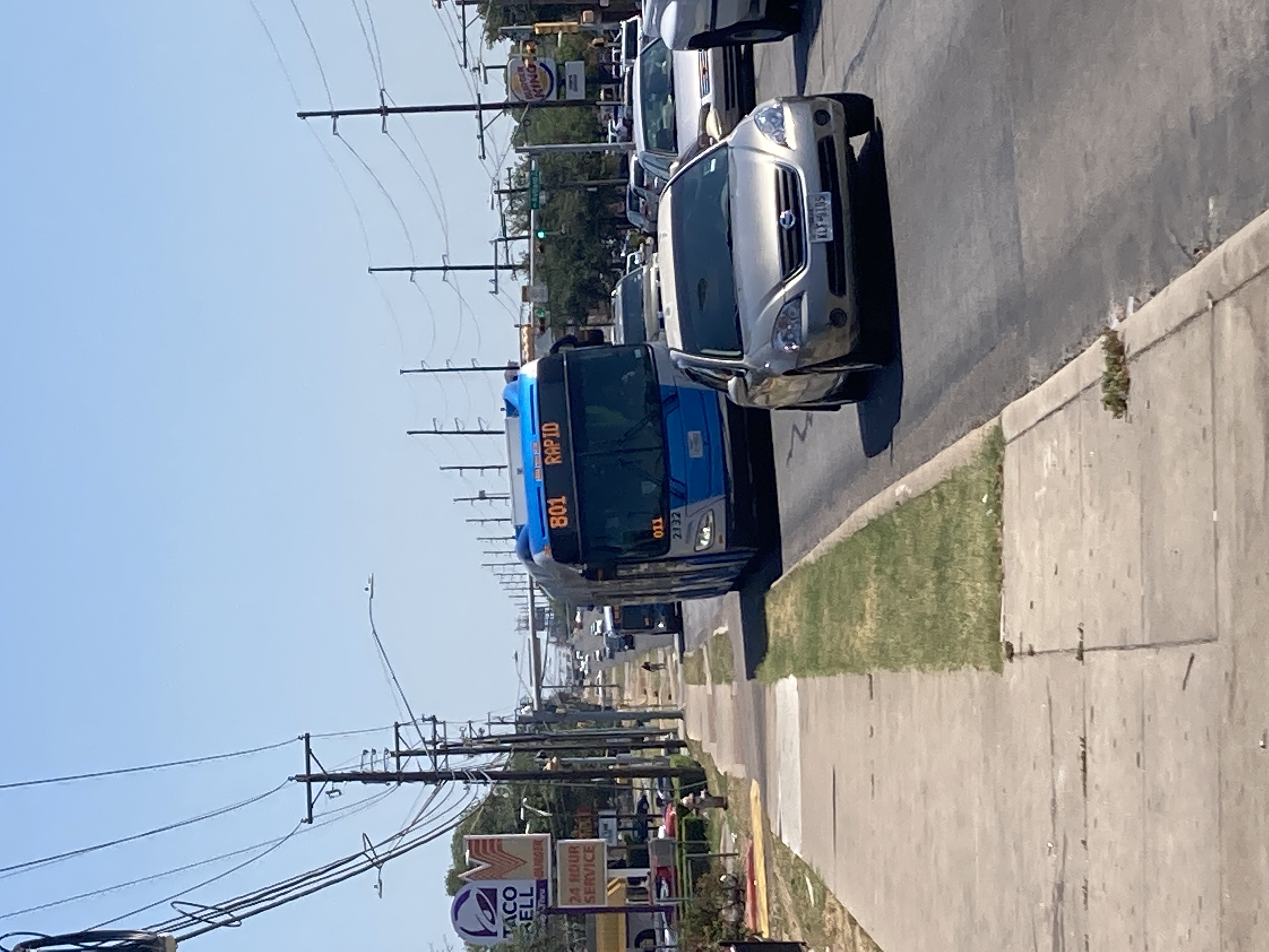 an articulated bus in traffic on a six lane street with telephone poles on either side. 