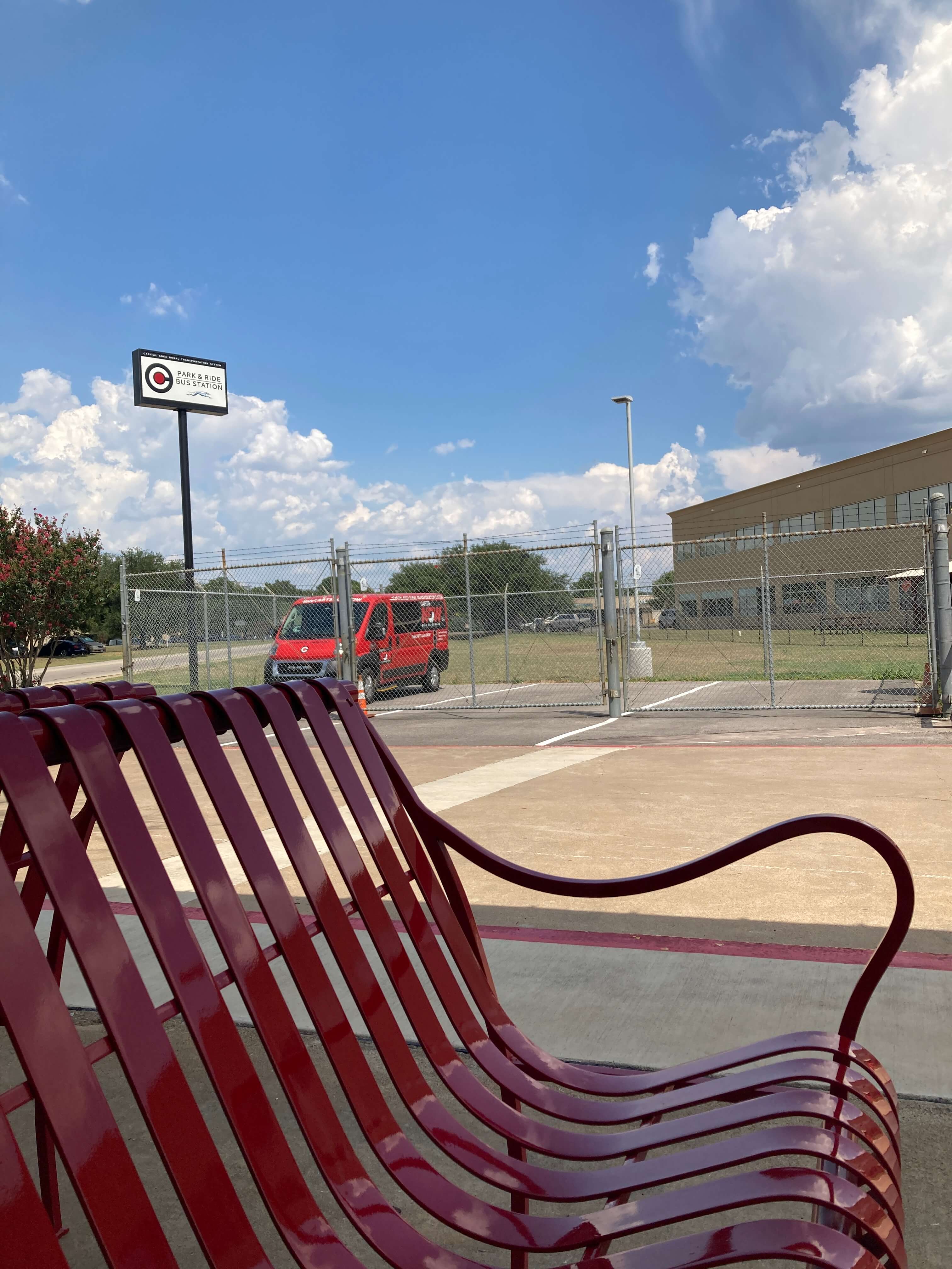 a ram promaster platform passenger van in bright red CARTS NOW livery sits inside a small fenced in area at the station.