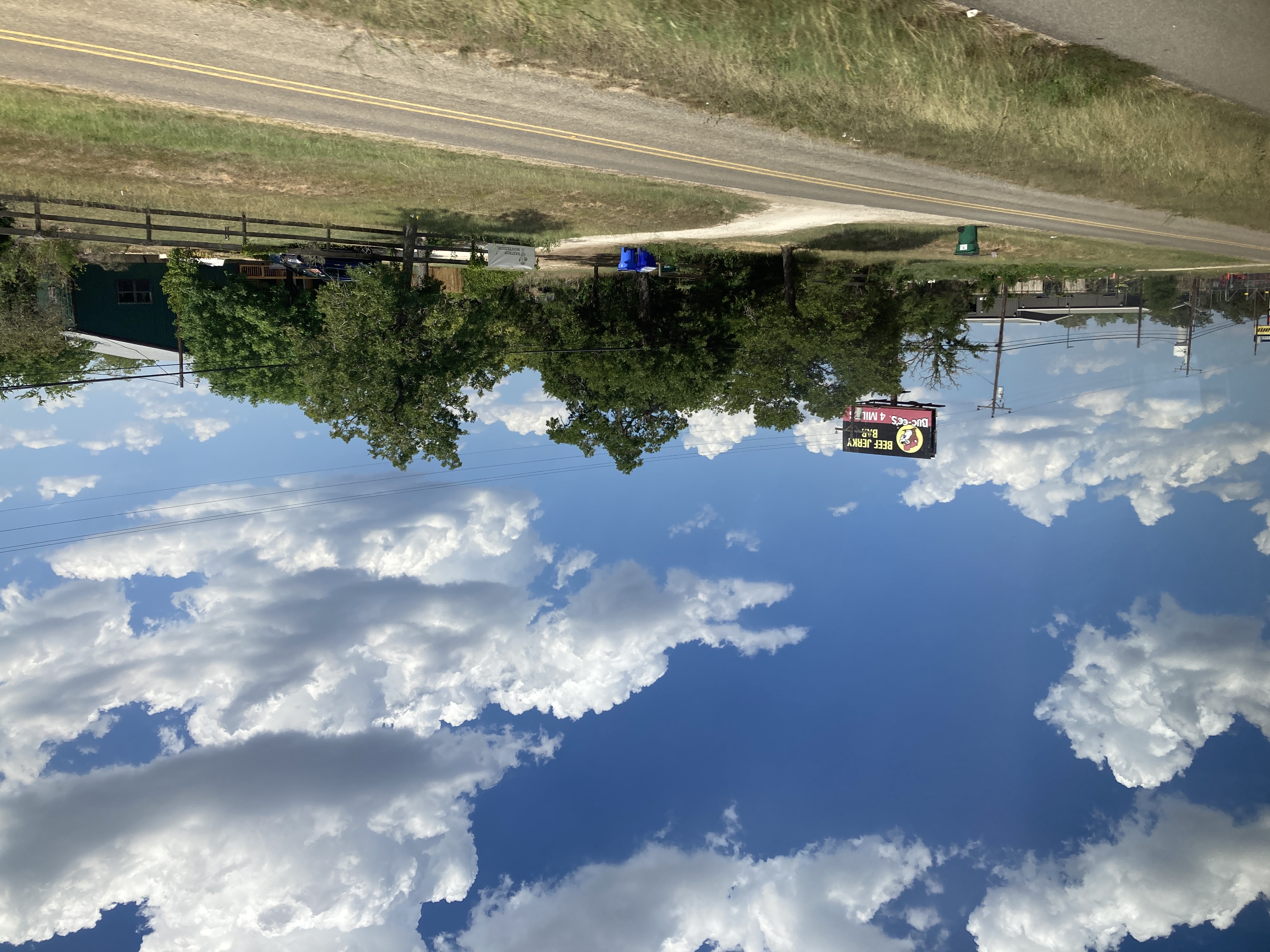 a buc-ees billboard reading Beef Jerky Bar looms over bushy trees and barns with dirt driveways 