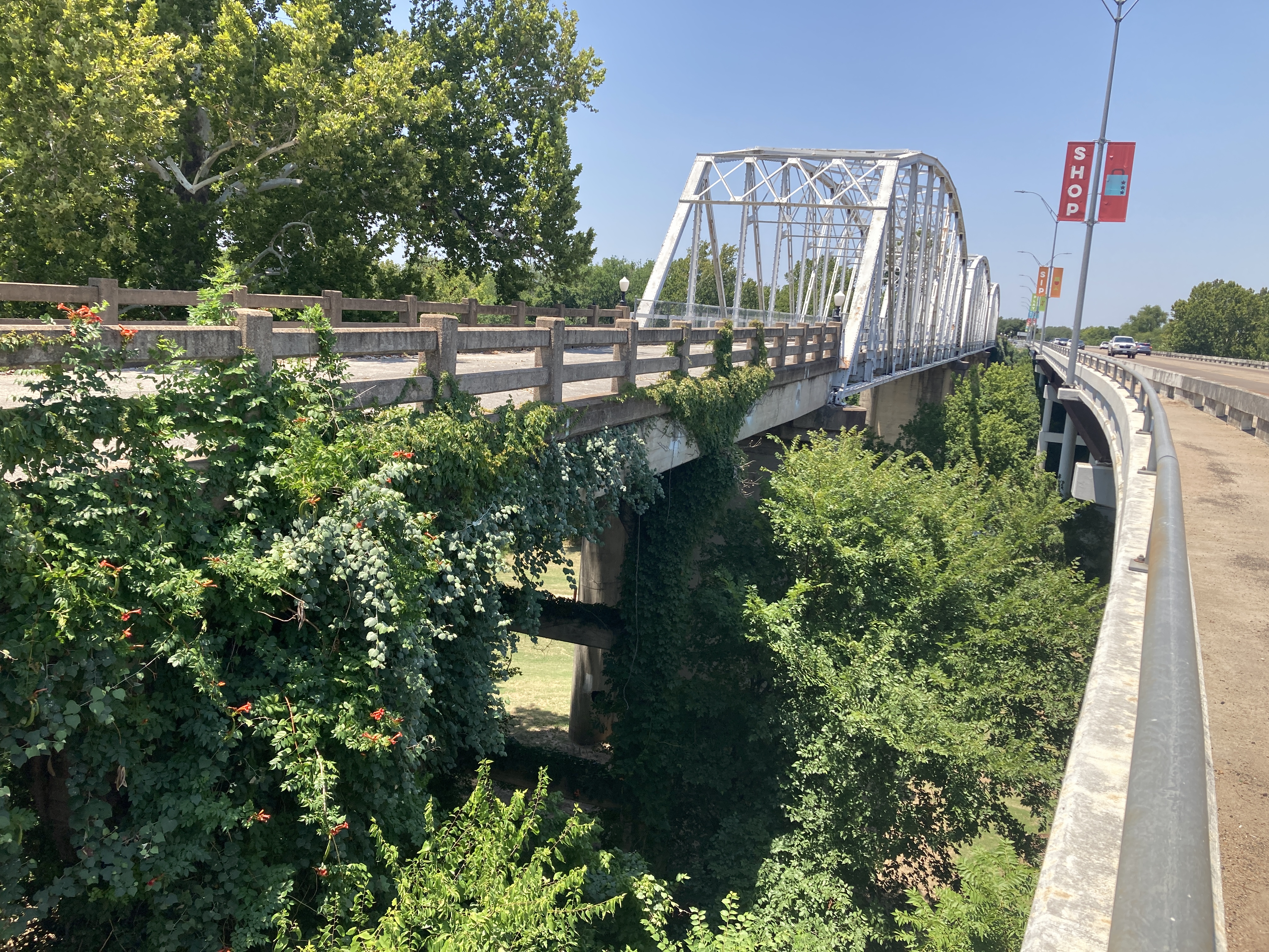 two bridges, one a simple concrete bridge and the other a disused, overgrown steel arch bridge 