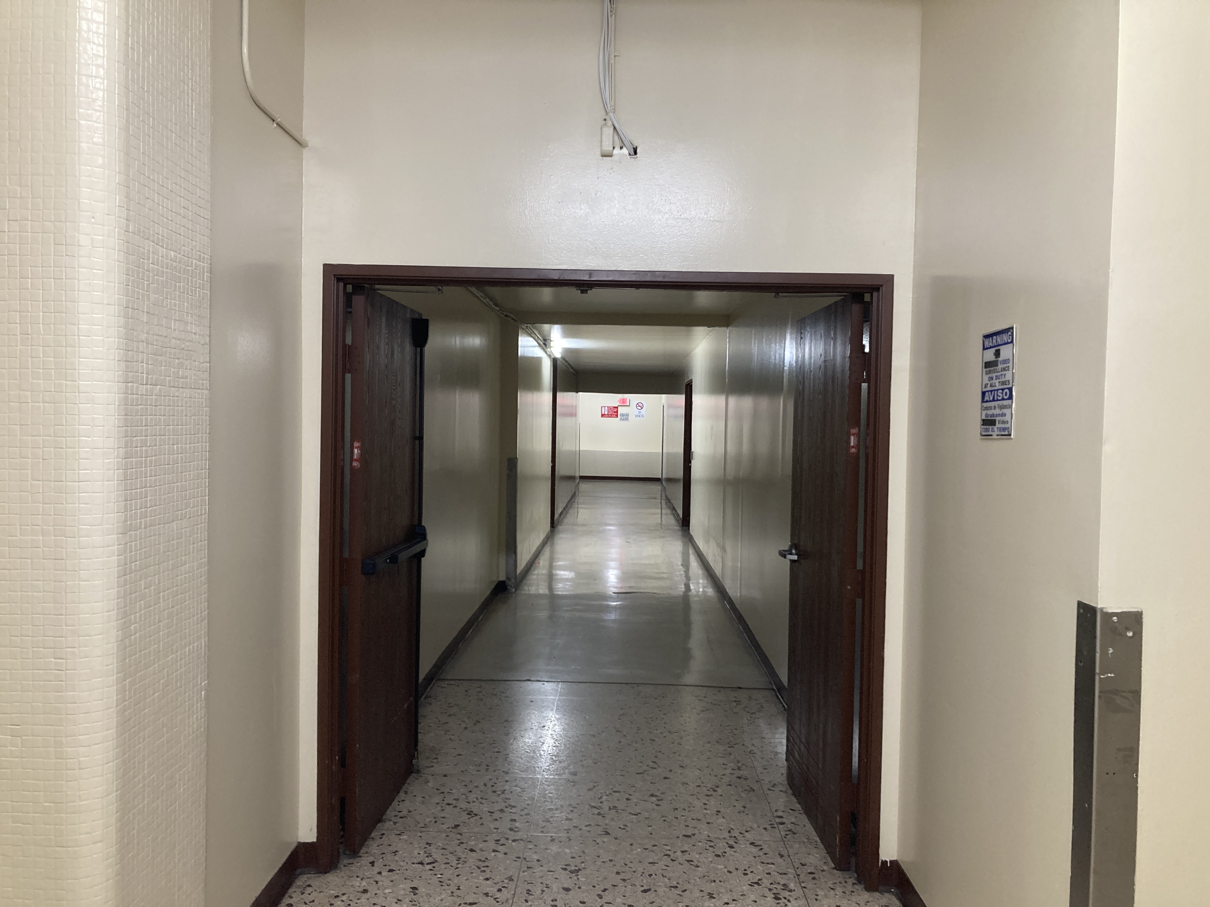 an interior hallway. there are rounded columns on the side, and it intersects with another hallway a few yards down. the floor is linoleum.