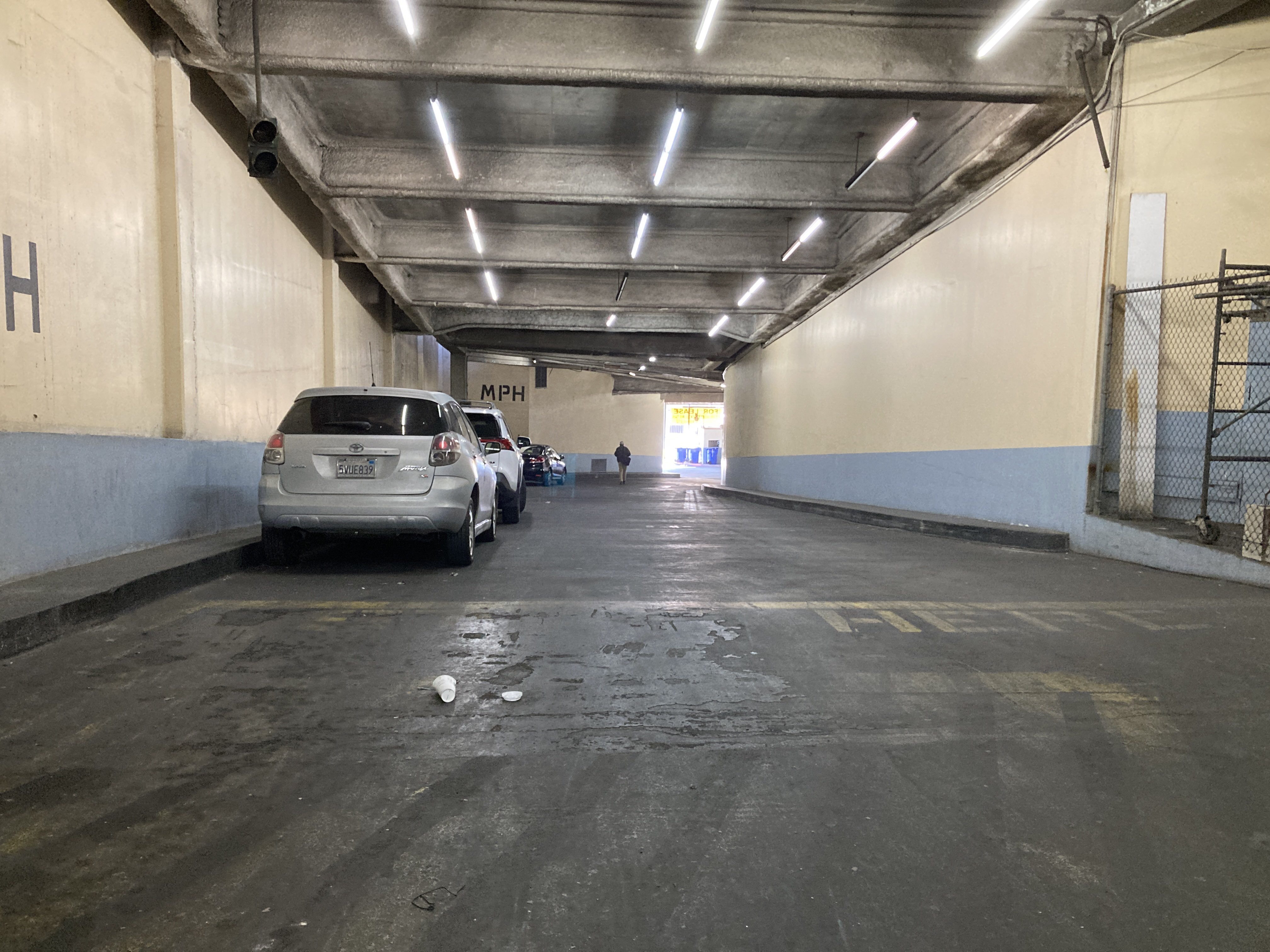 Looking down a large concrete ramp. cars are parked along the beige and powder blue walls, and large painted letters indicate the 5 mile per hour speed limit.