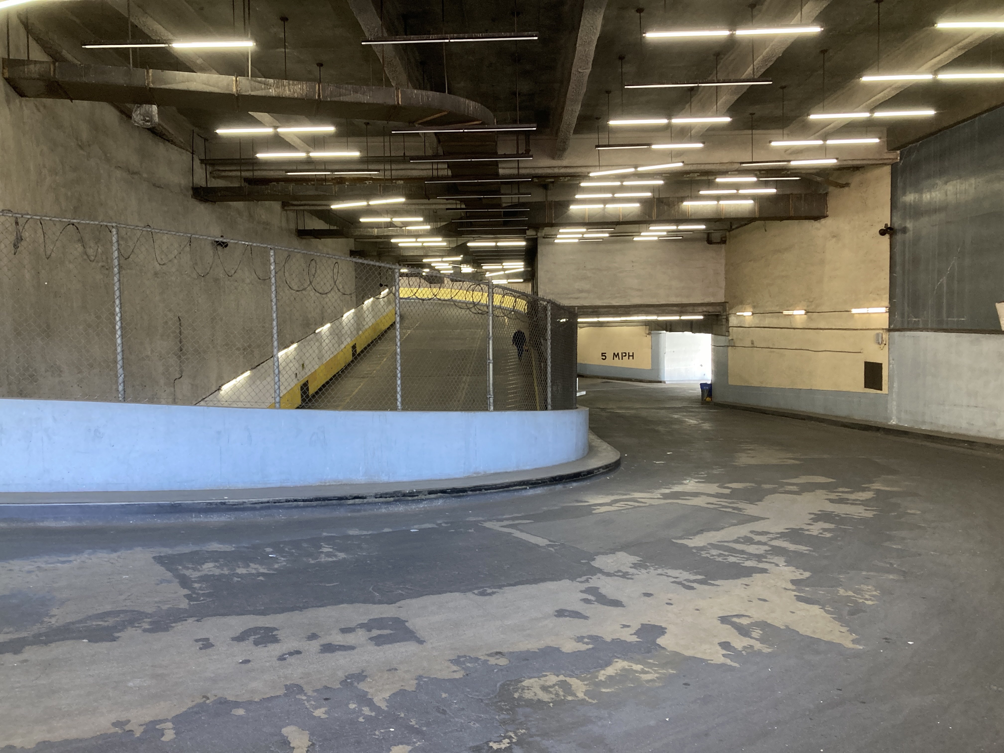 Interior open space with three vehicle ramps. one ramp goes from los angeles street up to the rooftop. it is separated by a chain length fence from two ramps that form a loop from seventh street to the second floor.