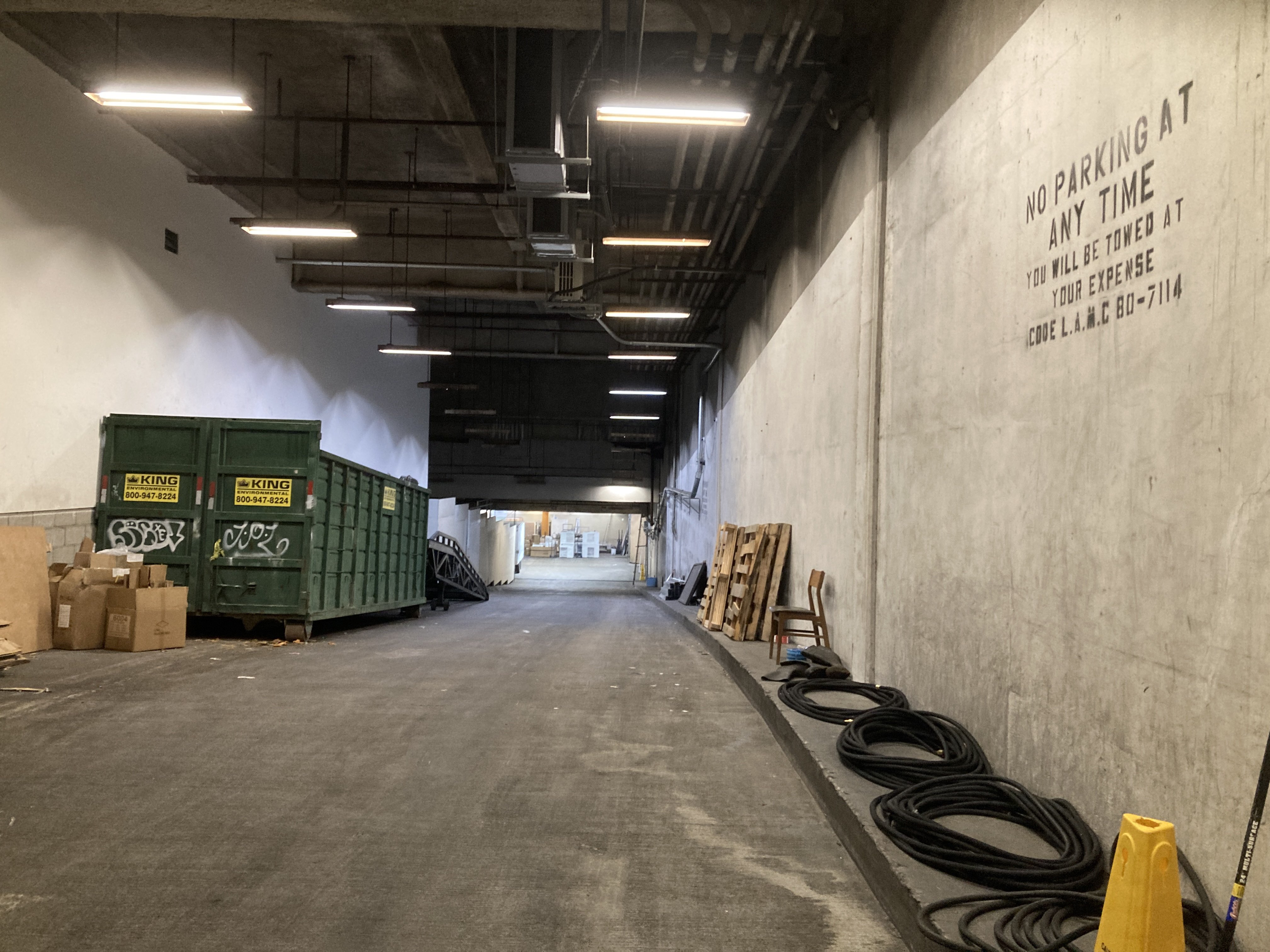 color photo looking into a ramp that goes down into a yellow-pillared room. a dumpster and some pallets are stored along the walls of the ramp.