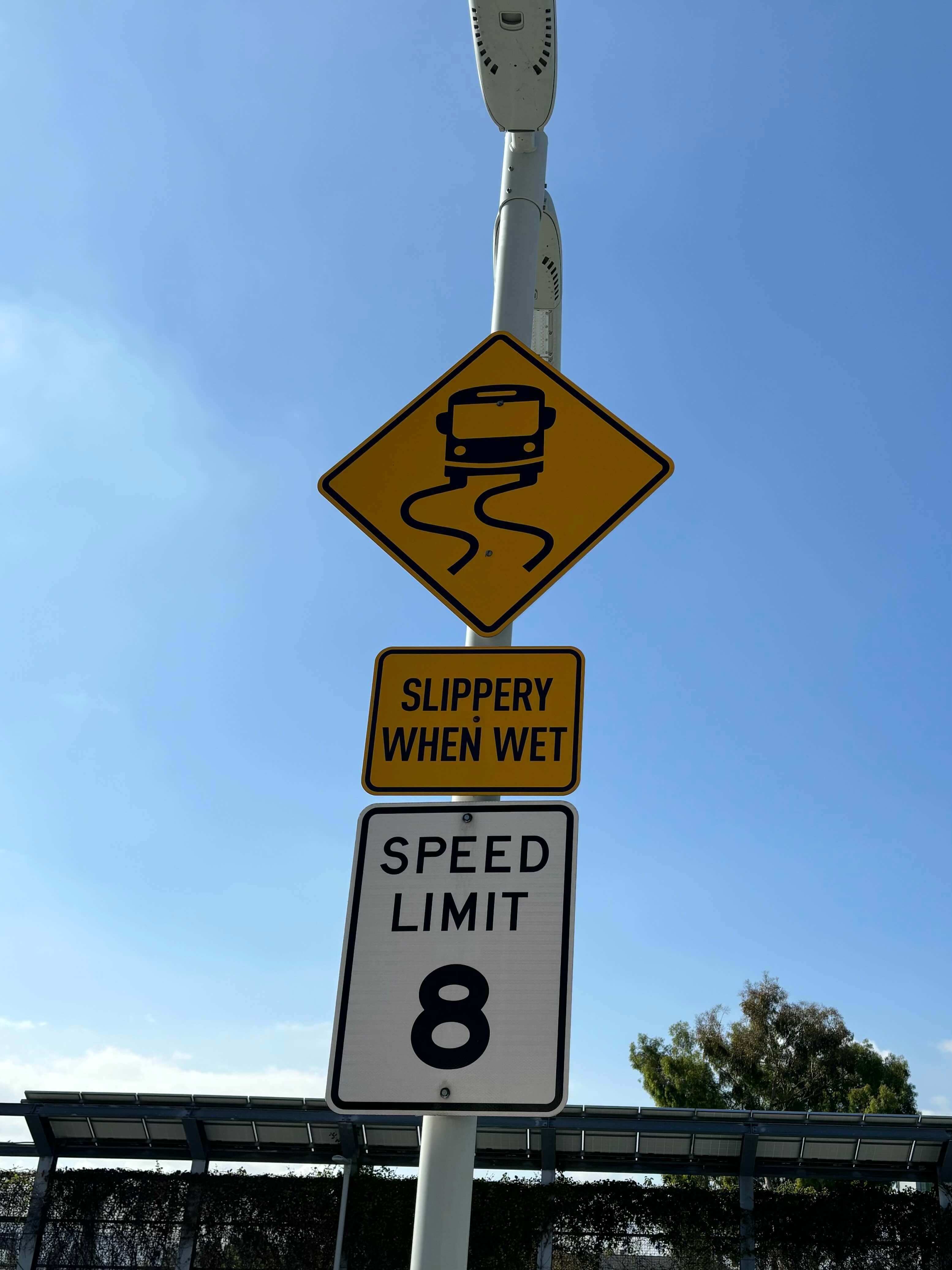 diamond shaped sign showing the simplified silhouette of a transit bus tracing s-shaped paths under its wheels. below the diamond is a rectangular sign reading, Slippery when wet