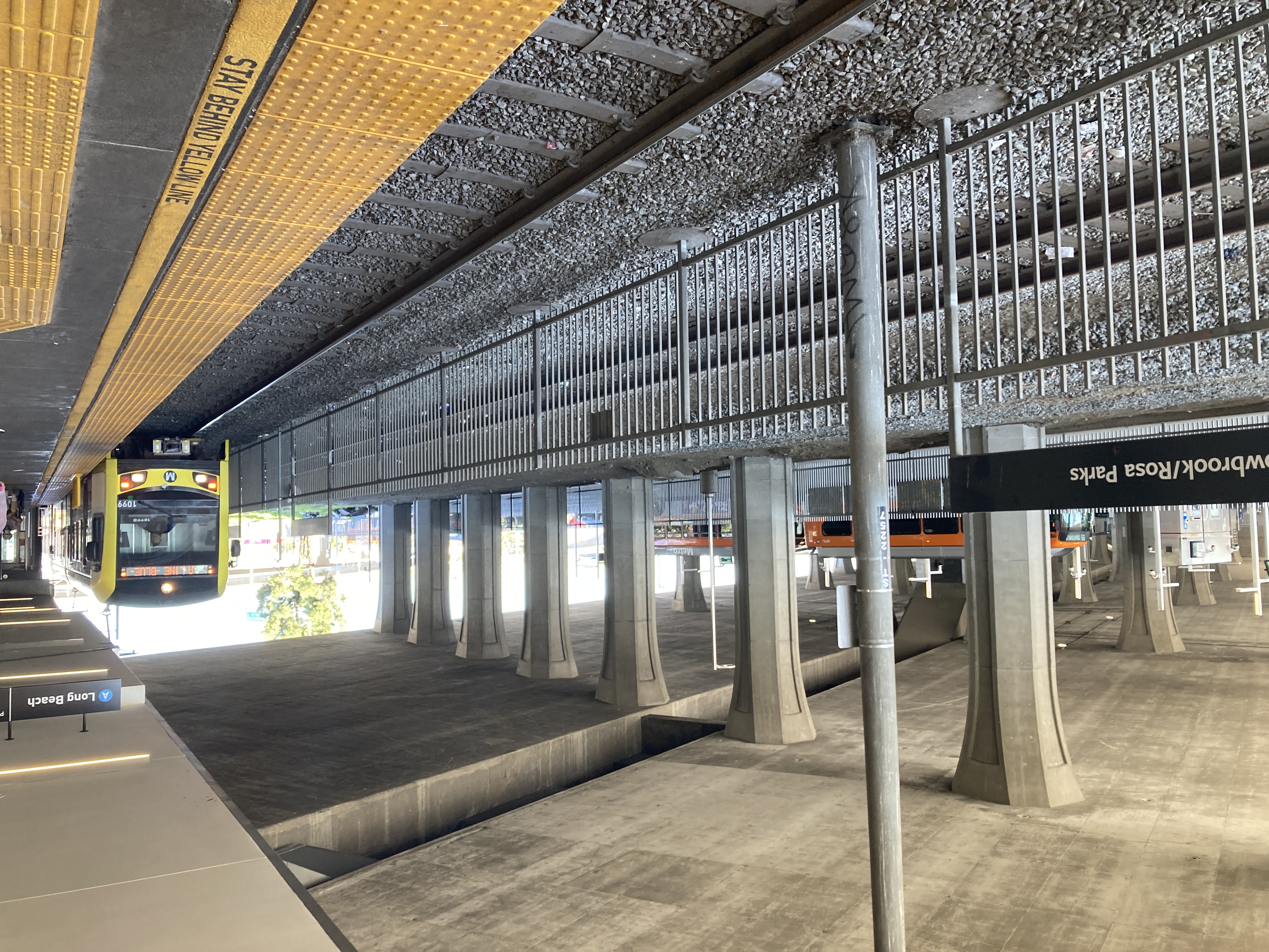 a p3010 train arrives southbound at the platform under the viaduct. across a fence and freight tracks from the light rail, a bus plaza with at least a dozen bays.